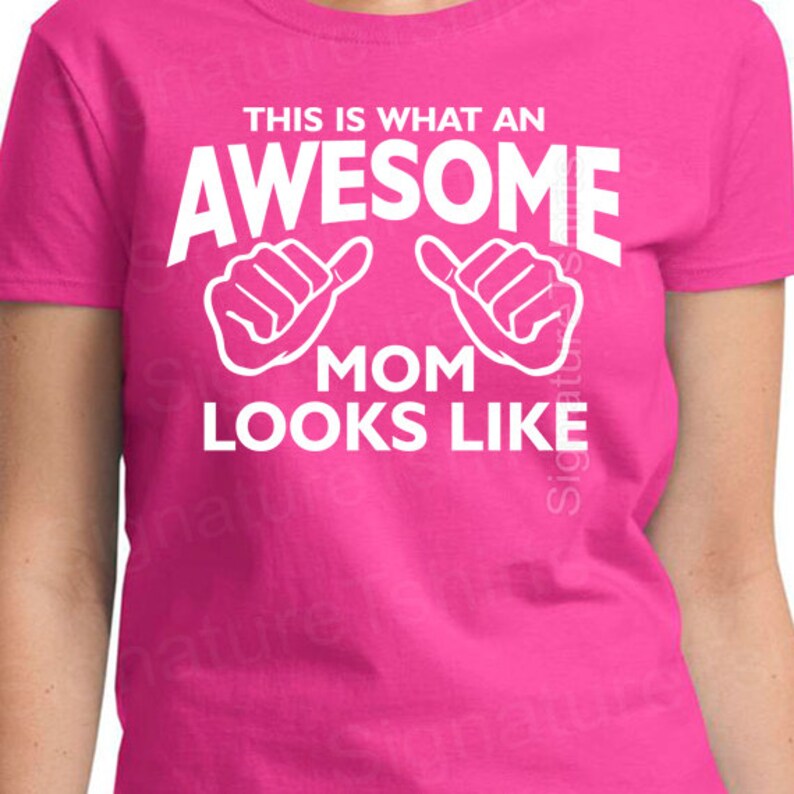 May include: Pink t-shirt with white text that reads "This is what an awesome mom looks like" with two thumbs up hand gestures.