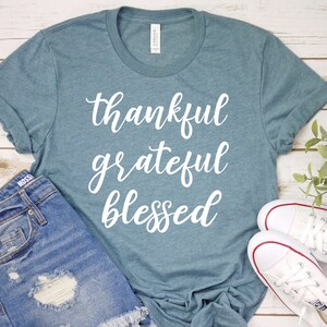 May include: A teal blue t-shirt with the words "thankful grateful blessed" written in white cursive lettering.