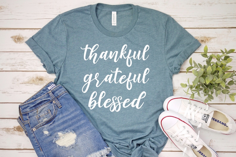 May include: A teal blue t-shirt with the words "thankful grateful blessed" written in white cursive lettering.