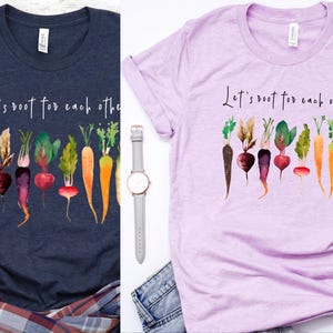 May include: Two t-shirts with the text "Let's root for each other" and a watercolor illustration of a row of carrots and beets. The shirts are navy blue and light purple.