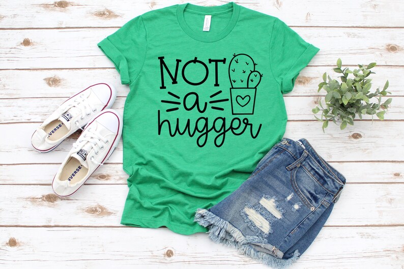 May include: Green t-shirt with the text "NOT a hugger" and a black and white illustration of a cactus in a pot with a heart.