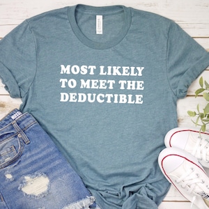 May include: A teal t-shirt with the text "MOST LIKELY TO MEET THE DEDUCTIBLE" in white, paired with denim shorts and white sneakers. The shirt is folded, and the sneakers are placed next to the shorts.