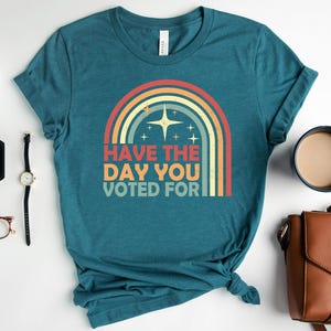 May include: Teal t-shirt with a retro rainbow graphic and the text "Have the day you voted for." The design features a star and stripes in a vintage style. The shirt is displayed with accessories.