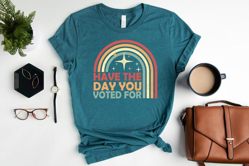 May include: Teal t-shirt with a retro rainbow graphic and the text "Have the day you voted for." The design features a star and stripes in a vintage style. The shirt is displayed with accessories.