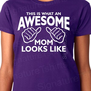 May include: Purple t-shirt with white text that reads "This is what an awesome mom looks like" with two white thumbs up symbols.