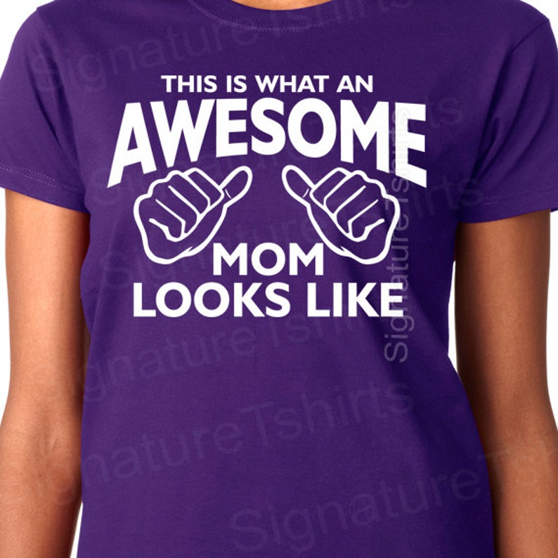 May include: Purple t-shirt with white text that reads "This is what an awesome mom looks like" with two white thumbs up symbols.
