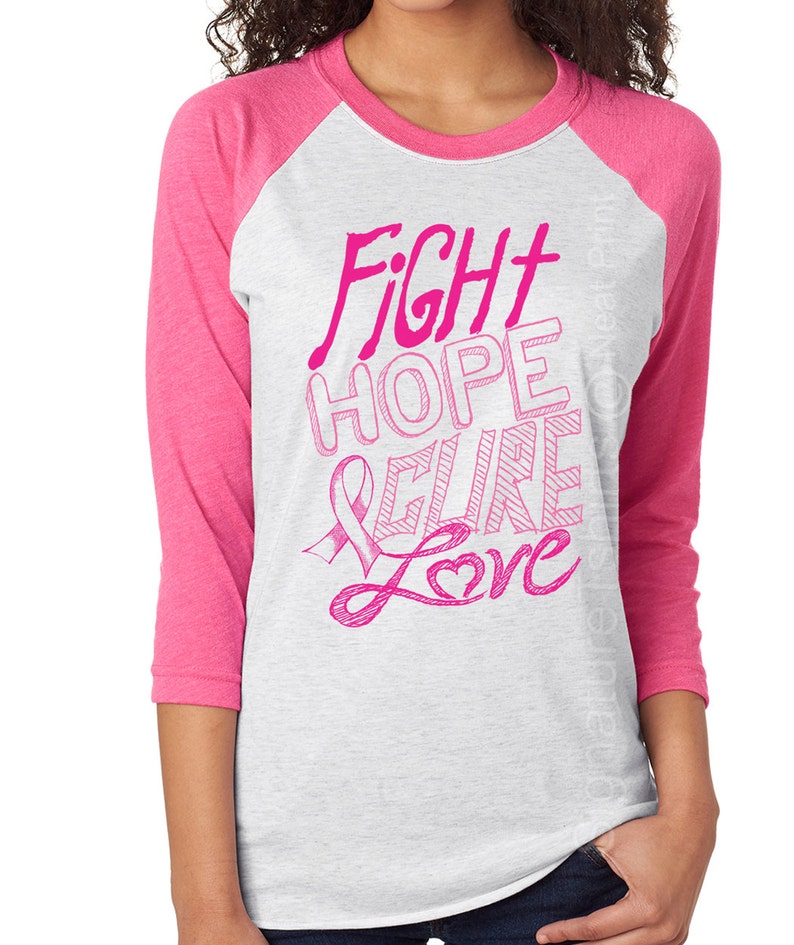 May include: A white and pink baseball tee shirt with a pink ribbon and the words "Fight Hope Cure Love" in pink.