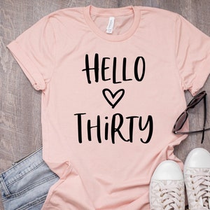 May include: A pink t-shirt with the text "HELLO THIRTY" in black lettering with a heart symbol between the words.