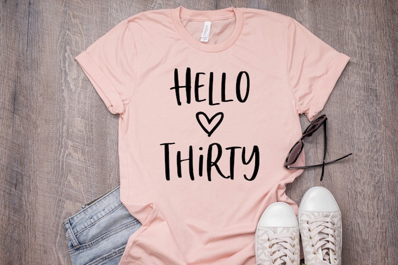 May include: A pink t-shirt with the text "HELLO THIRTY" in black lettering with a heart symbol between the words.
