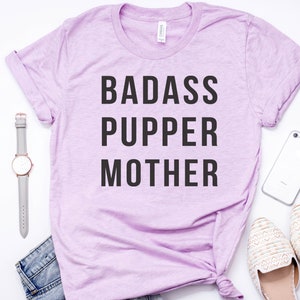 May include: A light purple t-shirt with the text "BADASS PUPPER MOTHER" printed in black.