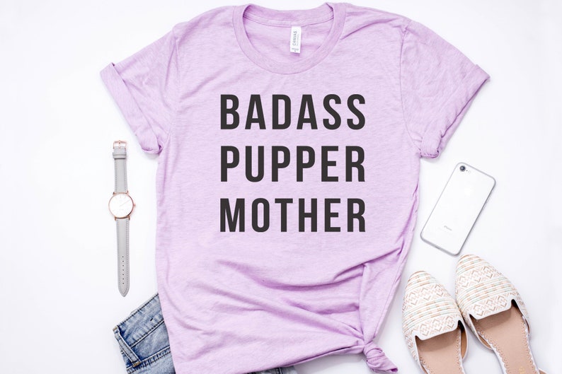 May include: A light purple t-shirt with the text "BADASS PUPPER MOTHER" printed in black.