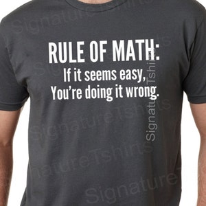 May include: A dark grey t-shirt with white text that reads "RULE OF MATH: If it seems easy, You're doing it wrong."