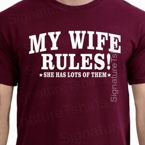 May include: Burgundy t-shirt with white text that reads "My Wife Rules!" and a star on either side of the text that reads "She has lots of them".