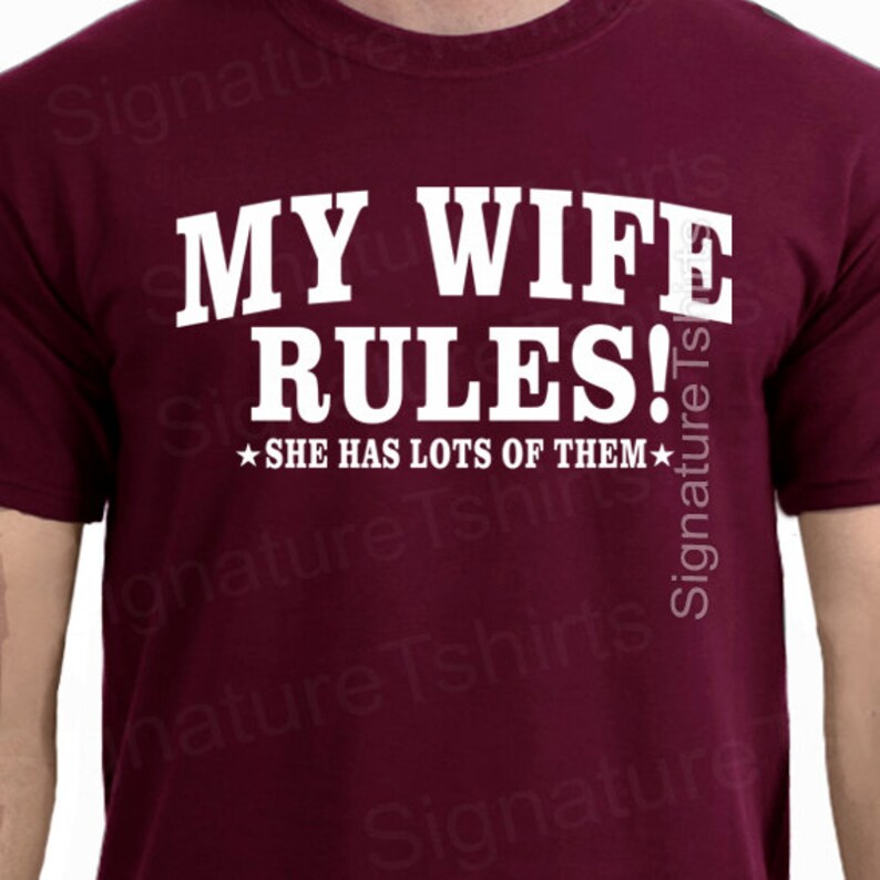 May include: Burgundy t-shirt with white text that reads "My Wife Rules!" and a star on either side of the text that reads "She has lots of them".
