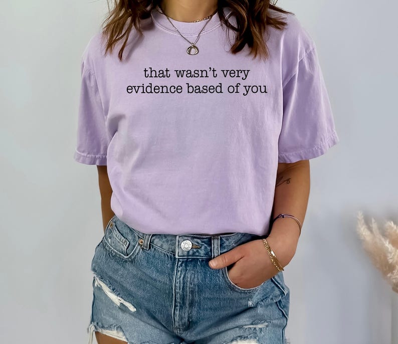 May include: A light purple t-shirt with the phrase "that wasn't very evidence based of you" printed in black. The shirt is paired with denim shorts.