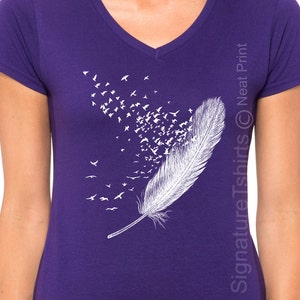 May include: Purple V-neck t-shirt with a white feather design. The feather is made up of a flock of birds flying away.