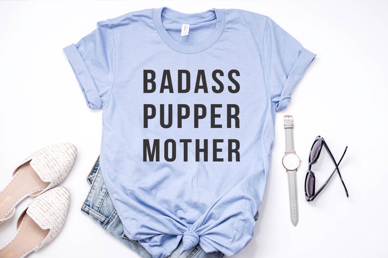 May include: A light blue t-shirt with the text "BADASS PUPPER MOTHER" printed in black.