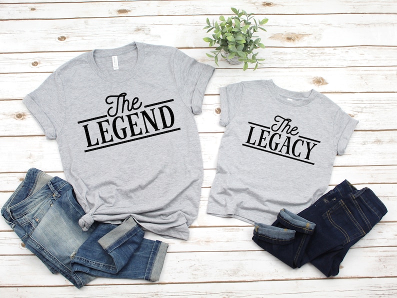 May include: Two gray t-shirts with black text. The larger shirt says "The Legend" and the smaller shirt says "The Legacy".