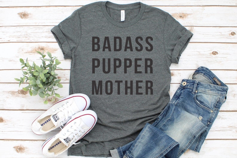 May include: A dark gray t-shirt with the text "BADASS PUPPER MOTHER" printed in black.