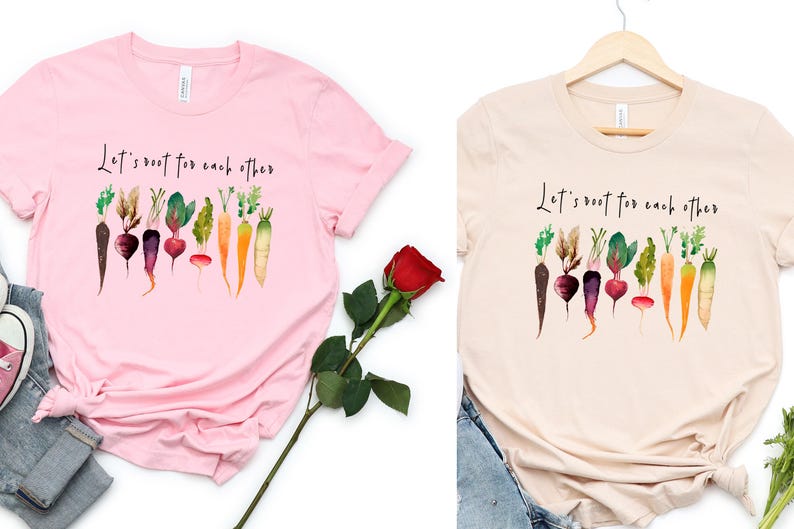 May include: Two t-shirts with a watercolor illustration of vegetables and the text "Let's root for each other". The shirts are pink and beige.