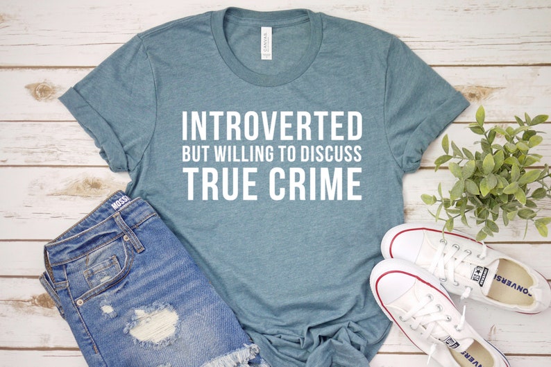 May include: A teal blue t-shirt with the text "Introverted but willing to discuss true crime" in white.