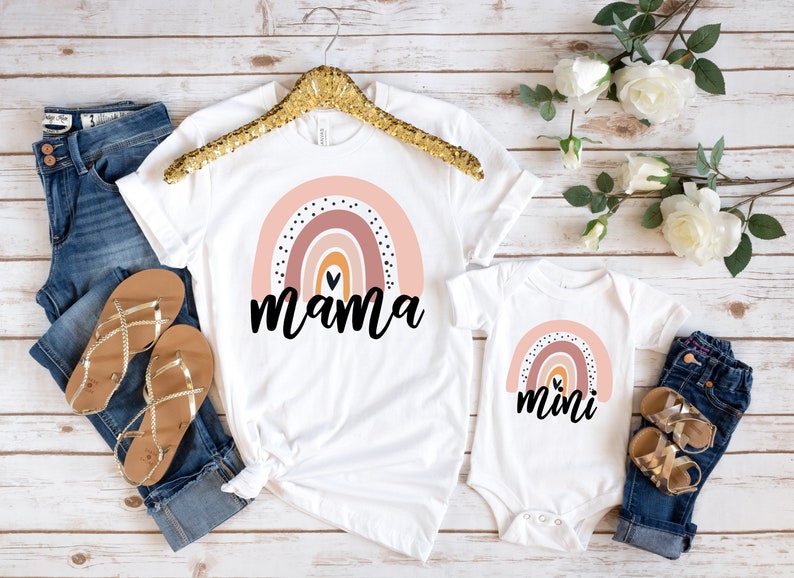 May include: A white t-shirt with a rainbow design and the word "mama" printed on it. A white onesie with a rainbow design and the word "mini" printed on it.