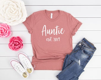 Op de afbeelding: Een stoffig roze T-shirt met de tekst "Auntie est. 2019" in wit.