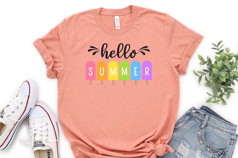 May include: A peach colored t-shirt with the text "hello summer" in black lettering. The text is surrounded by six colorful popsicle graphics.