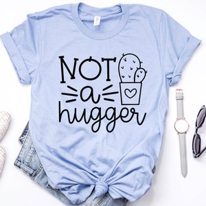 May include: A light blue t-shirt with the text "NOT a hugger" and a black and white illustration of a cactus in a pot.
