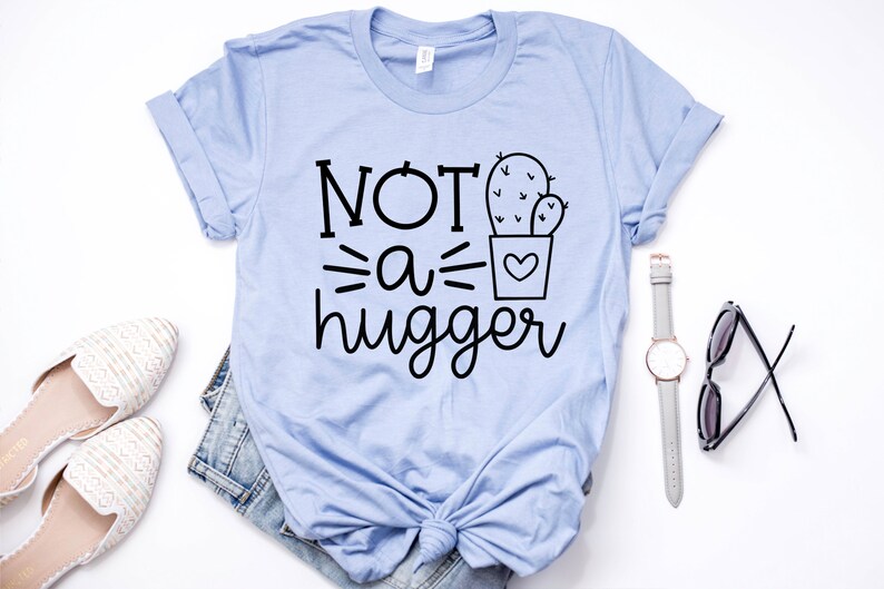 May include: A light blue t-shirt with the text "NOT a hugger" and a black and white illustration of a cactus in a pot.
