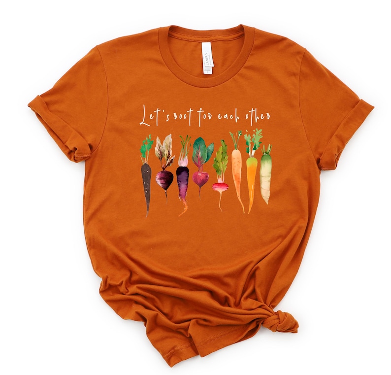 May include: Orange short-sleeved t-shirt with the text "Let's root for each other" and a watercolor illustration of various vegetables, including carrots, beets, and turnips.