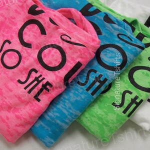 May include: Four t-shirts in different colors with the text "She's So Cool" printed on them. The shirts are stacked on top of each other, with the pink shirt on top and the white shirt on the bottom.