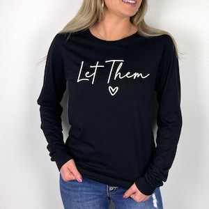May include: Black long-sleeve shirt with white text that reads "Let Them" and a small heart.