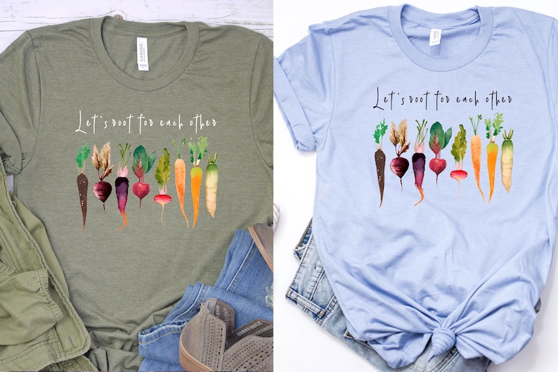 May include: Two t-shirts with a green and a light blue background. Both shirts feature a watercolor illustration of vegetables with the text "Let's root for each other".