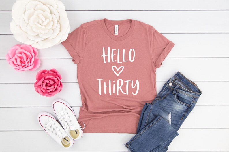May include: A dusty rose colored t-shirt with the text "HELLO THIRTY" in white with a heart symbol between the words.
