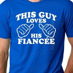 May include: A royal blue t-shirt with white text that reads "This Guy Loves His Fiancée" with two white thumbs up symbols.