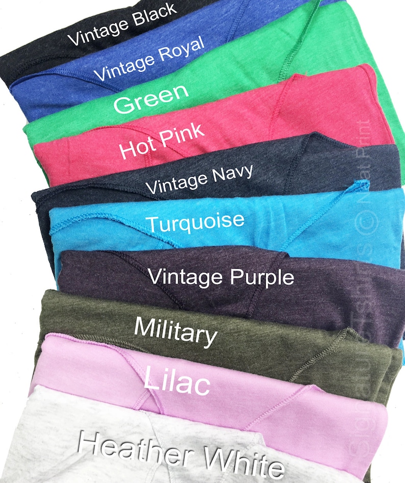 May include: A stack of folded t-shirts in various colors, including vintage black, vintage royal, green, hot pink, vintage navy, turquoise, vintage purple, military, lilac, and heather white.