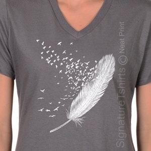 May include: Gray V-neck t-shirt with a white graphic of a feather with birds flying out of it. The text "Signature Tshirts &copy; Neat Print" is on the right side of the shirt.