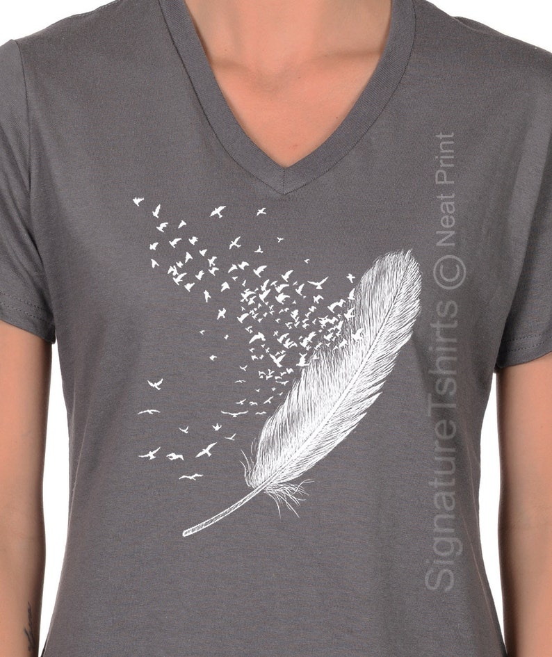 May include: Gray V-neck t-shirt with a white graphic of a feather with birds flying out of it. The text "Signature Tshirts &copy; Neat Print" is on the right side of the shirt.