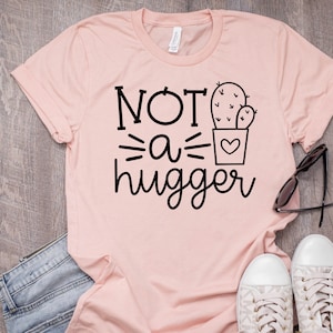 May include: A pink t-shirt with the text "NOT a hugger" and a cactus graphic.