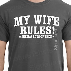 May include: A dark gray t-shirt with white text that reads "My Wife Rules!" and a small star on either side of the text that reads "She has lots of them."