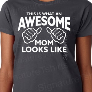 May include: A dark gray t-shirt with white text that reads "This is what an awesome mom looks like" with two white thumbs up symbols.
