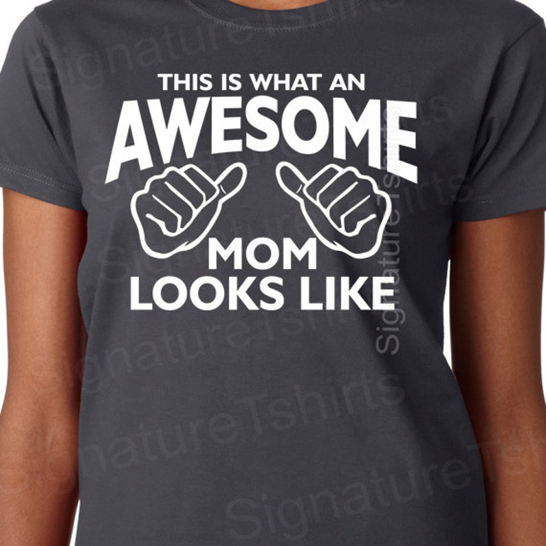 May include: A dark gray t-shirt with white text that reads "This is what an awesome mom looks like" with two white thumbs up symbols.