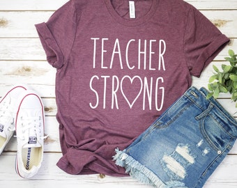 May include: A maroon t-shirt with the text "TEACHER STRONG" in white with a heart in the middle of the word "STRONG".