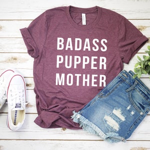 May include: A maroon t-shirt with the text "BADASS PUPPER MOTHER" in white lettering.