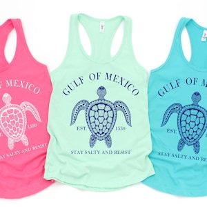 May include: Three tank tops with a sea turtle graphic and the text "Gulf of Mexico Est. 1550 Stay Salty and Resist". The tank tops are pink, light green, and turquoise.