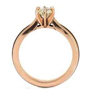 May include: A rose gold engagement ring with a single round diamond set in a prong setting. The band is a simple, polished design.