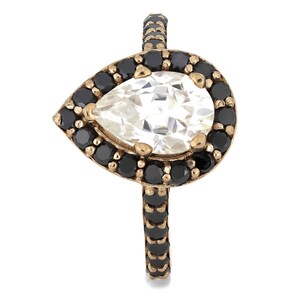 May include: A pear-shaped ring with a large clear stone surrounded by a halo of black stones. The band of the ring is also set with black stones.