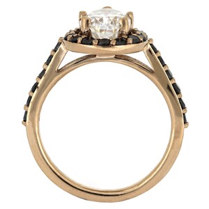May include: A rose gold ring with a large, clear center stone surrounded by a halo of black stones. The band is also set with black stones.