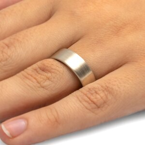 May include: A brushed silver wedding band worn on a finger.